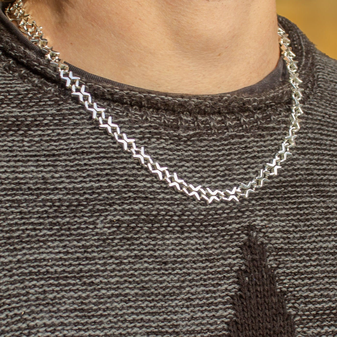 Close-up of a person wearing a silver chain necklace on a dark gray sweater.