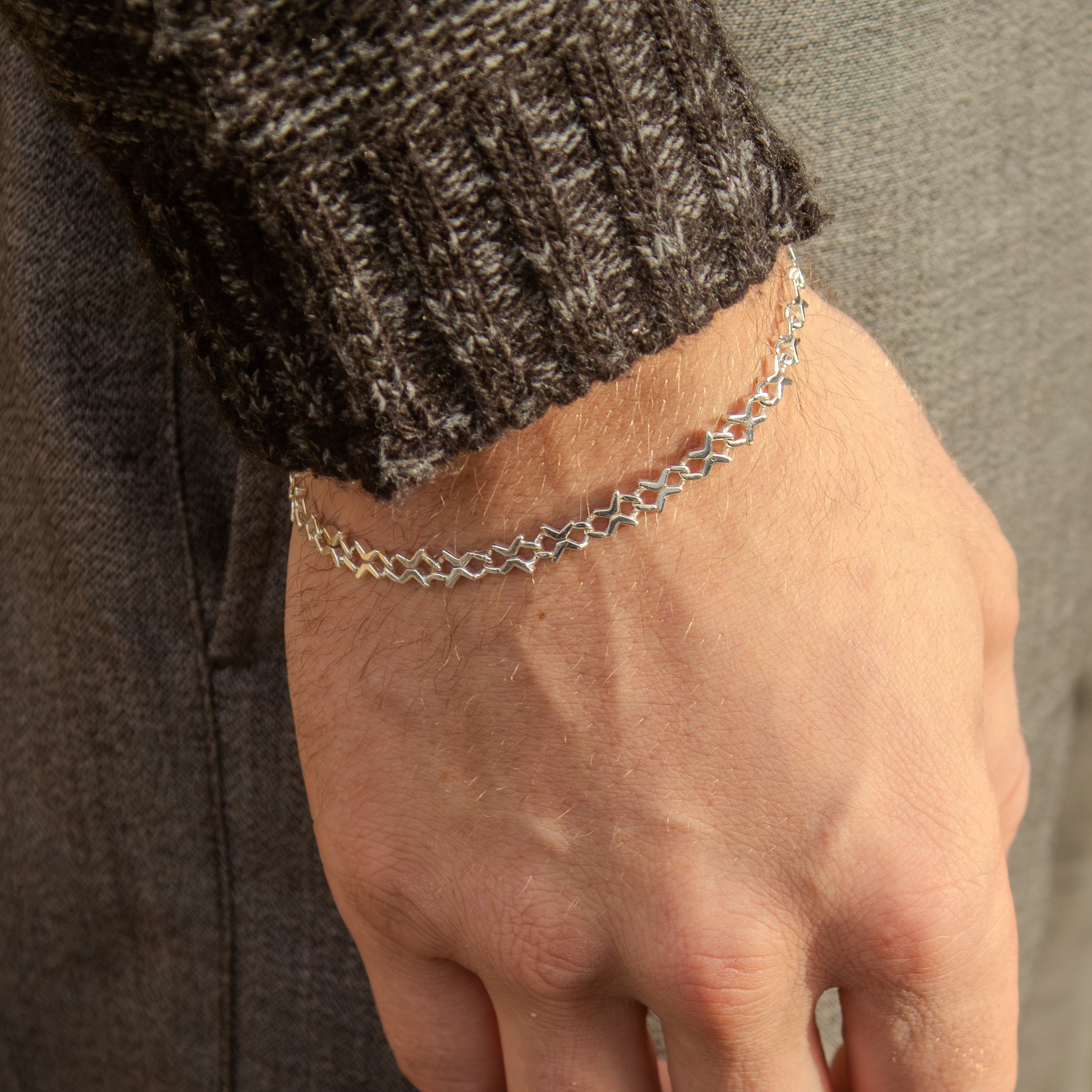 Hand wearing a silver chain bracelet with a neutral background